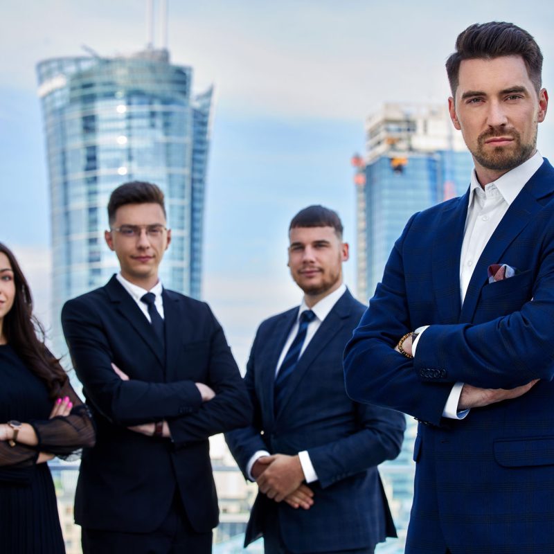 Czworo biznesmenów stoi przed drapaczami chmur w mieście. Biznes, sukces, praca zespołowa.