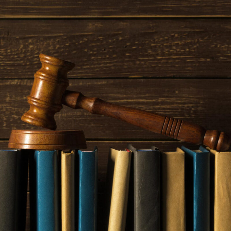 Drewniany młotek spoczywający na książkach prawniczych na tle drewna. Koncepcja prawa i sprawiedliwości.